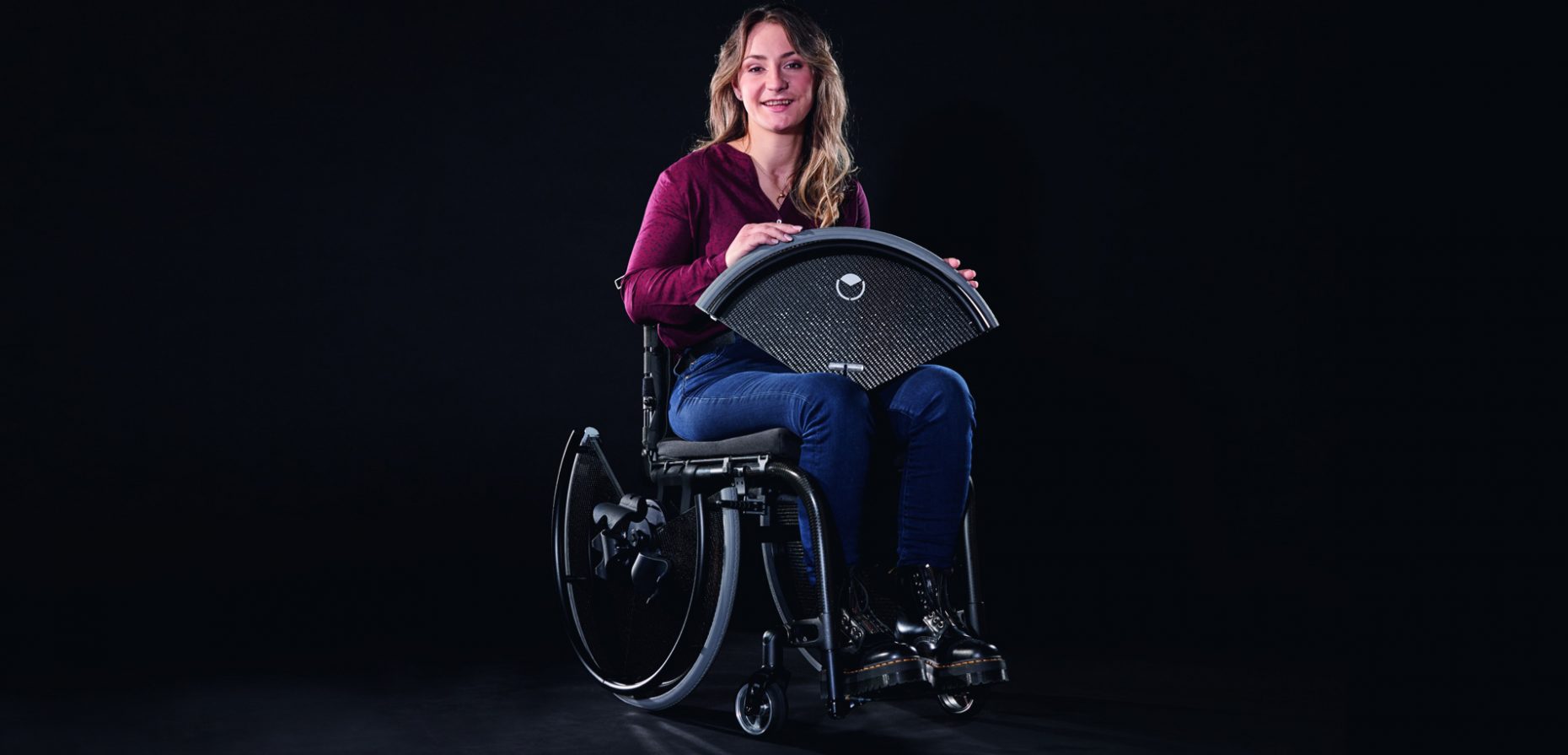 Das Foto zeigt die Trivida-Markenbotschafterin Kristina Vogel mit ihrem dank zweier Trivida-Räder barrierefrei gewordenen Rollstuhl. In ihrer Hand deutlich zu erkennen: das abgelöste obere Radsegment des Carbonscheibenrades.