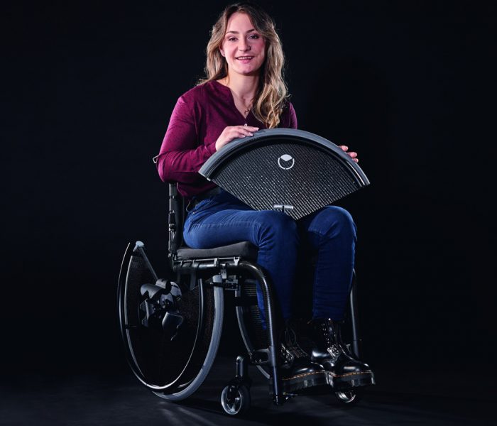Das Foto zeigt die Trivida-Markenbotschafterin Kristina Vogel mit ihrem dank zweier Trivida-Räder barrierefrei gewordenen Rollstuhl. In ihrer Hand deutlich zu erkennen: das abgelöste obere Radsegment des Carbonscheibenrades.